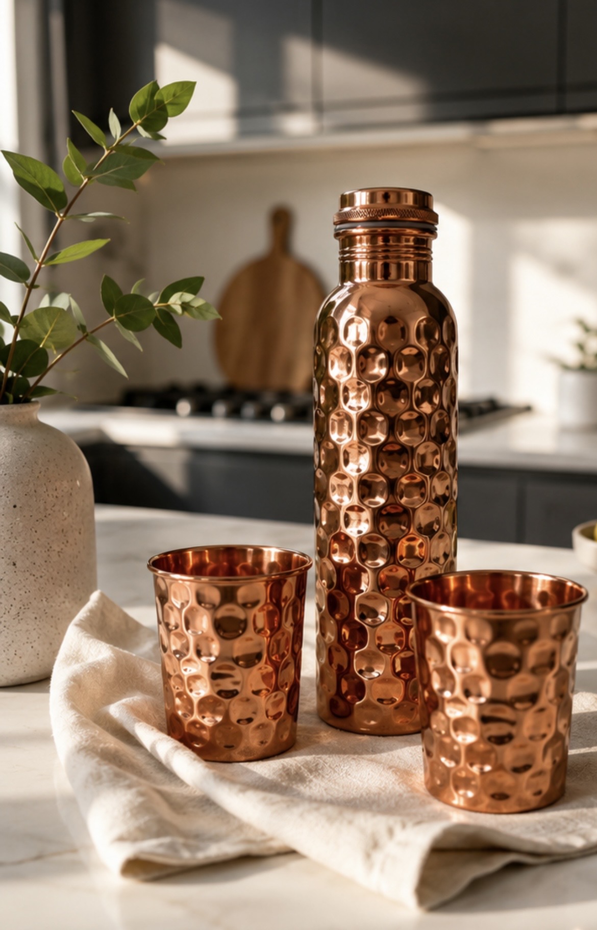 Hammered copper bottle and two matching cups in a modern kitchen